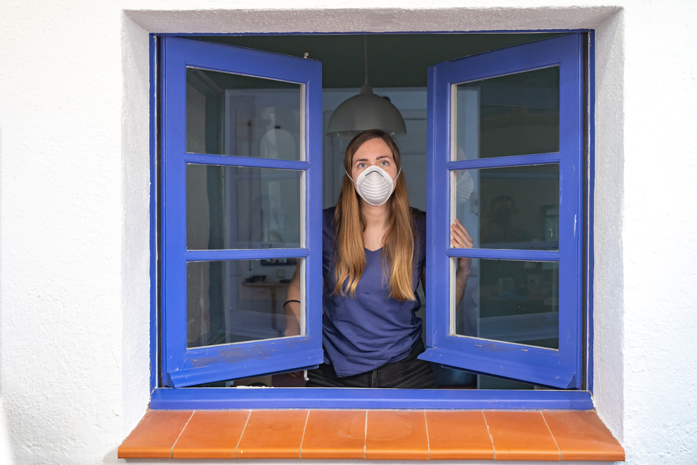 O femeie infectată cu COVID-19 se uită pe geam/ Foto: depositphotos.com