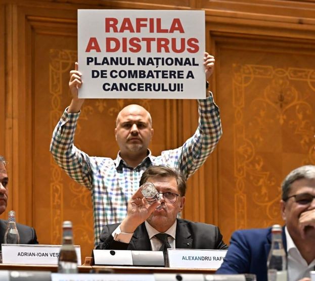 Emanuel Ungureanu, fotografiat în timp ce ținea o pancartă în spatele ministrului Alexandru Rafila, în Parlament / Foto: Facebook - Emanuel Ungureanu