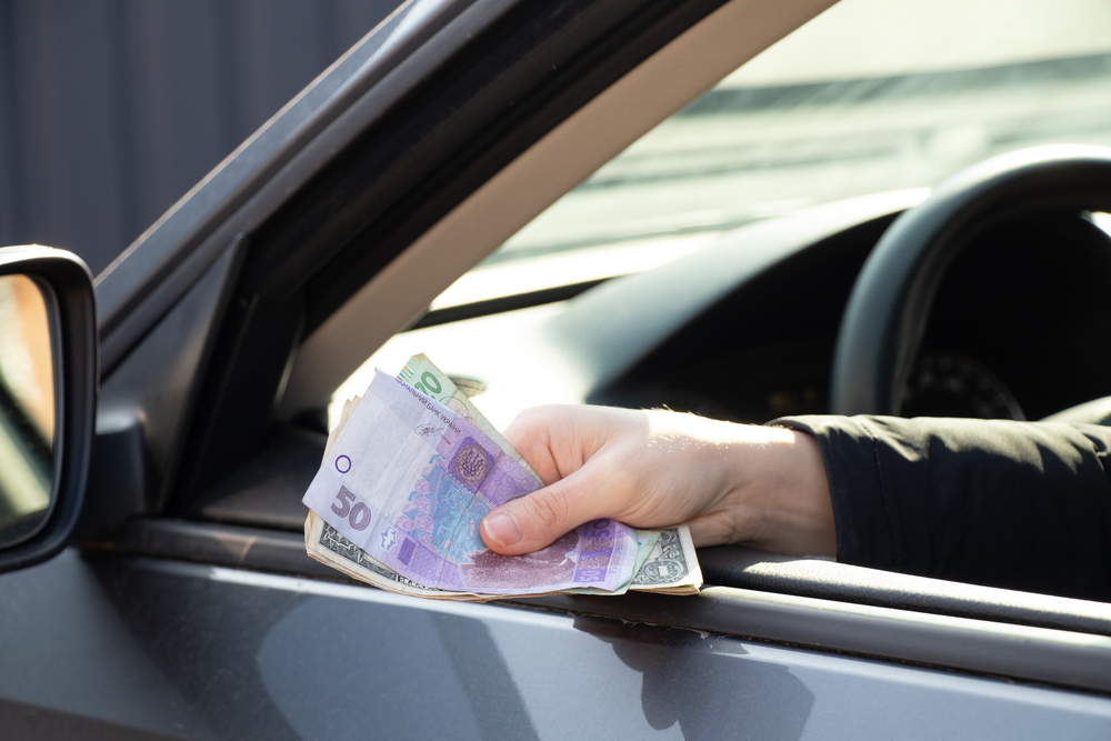 Mâna unei persoane care scoate bani de pe fereastra mașinii pentru a da mită/ Foto sugestivă: depositphotos.com