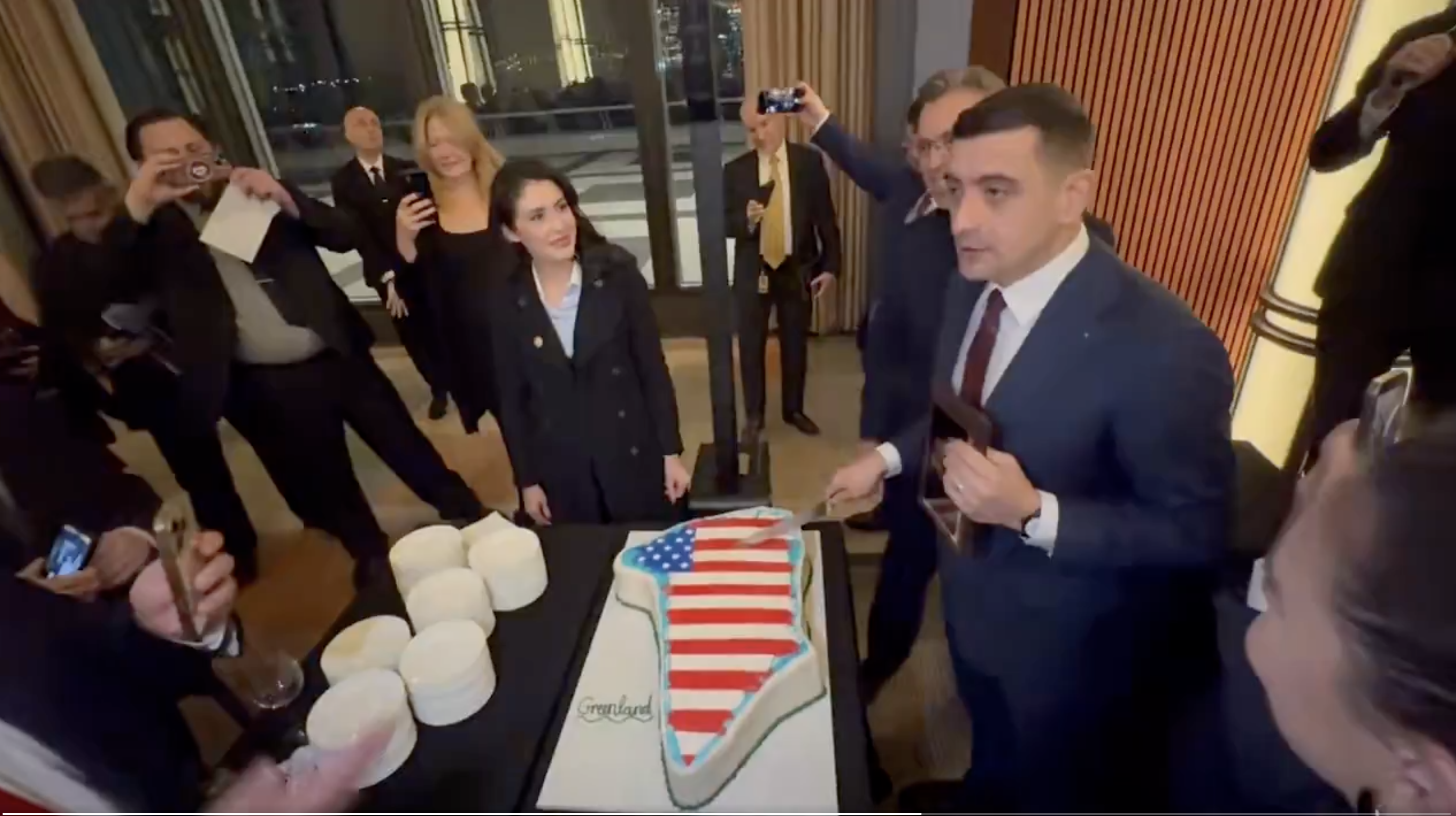 George Simion (AUR), în timp ce taie un tort cu forma Groenlndei | Foto: Captură video X (ex Twitter) - Mark Naughton